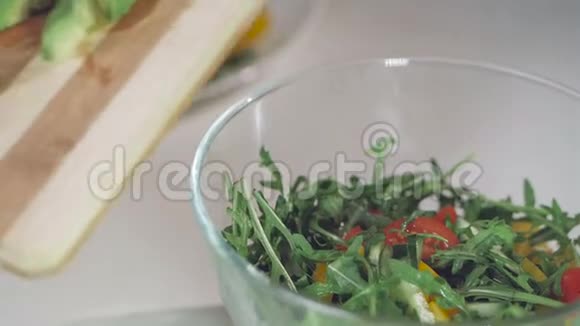 一个女人用玻璃碗折叠蔬菜沙拉原料的手的特写视频的预览图