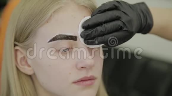 在染色程序后用棉盘擦拭一个年轻女孩的眉毛视频的预览图