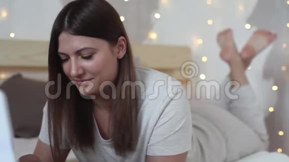 漂亮的女孩喜欢躺在床上的笔记本电脑特写视频的预览图