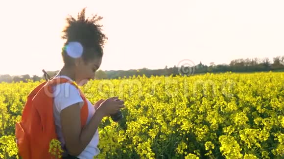 非洲裔美国少女女青年带着红色背包和相机在种子黄流领域拍照视频的预览图