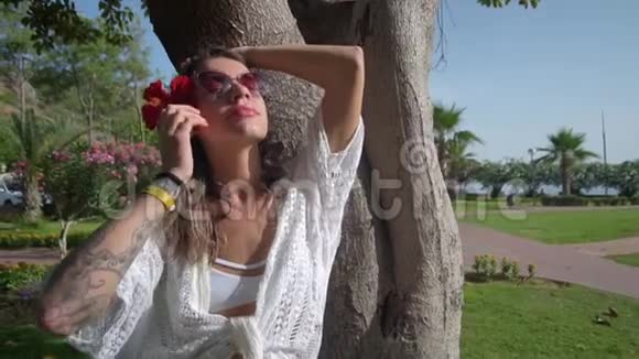 一个头上戴着一朵红花的女人站在一棵棕榈树附近看着太阳视频的预览图