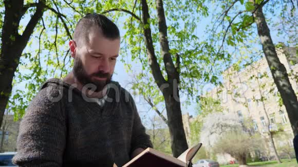 那个留胡子的人坐在公园里读一本有趣的书视频的预览图
