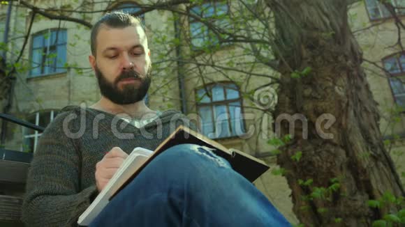 在一个阳光明媚的早晨学生坐在树旁边的公园里读一本书写一写视频的预览图