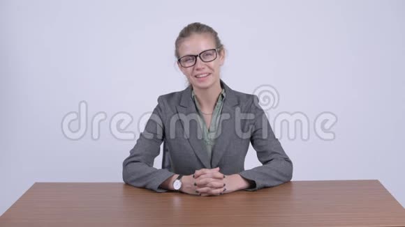年轻快乐的金发女商人微笑着坐在办公桌后面视频的预览图