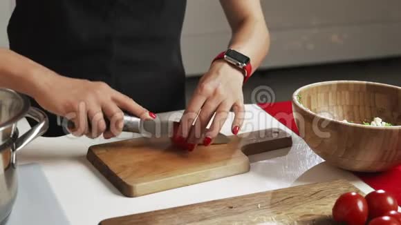 公寓里的厨房年轻女子用刀子在木板上切西红柿餐桌上切蔬菜视频的预览图