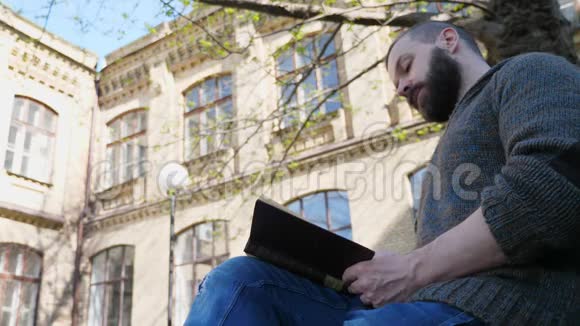 一个快乐的留胡子的人正在城市公园里休息他正在看书视频的预览图