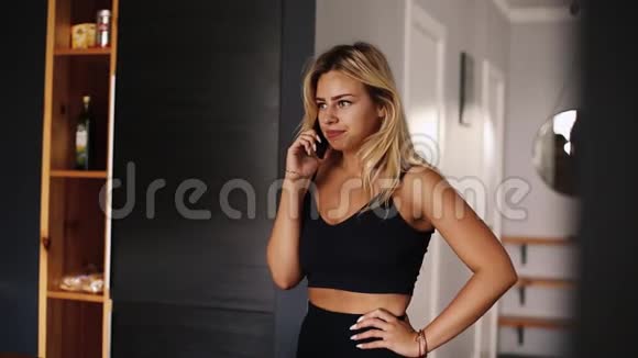 性感漂亮的金发女人走在家里用智能手机说话视频的预览图