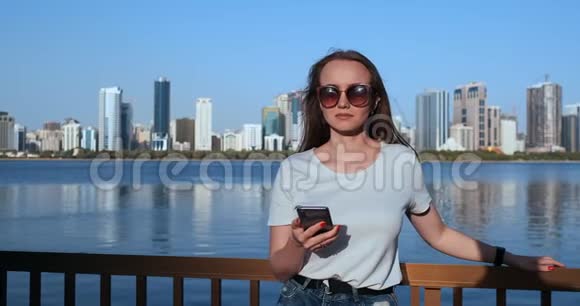 夏天的女孩站在一个大城市的背景下微笑着站在智能手机上视频的预览图