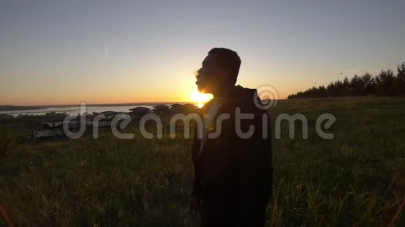 年轻的非裔美国人在美丽的夕阳下在夏日草地上抽烟视频的预览图