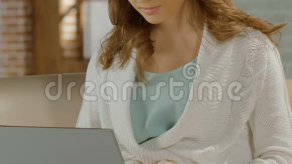 年轻女性坐在沙发上在笔记本电脑上打字微笑着约会网站视频的预览图