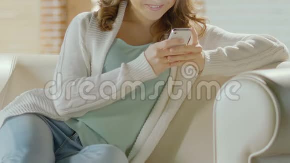 年轻迷人的女人在沙发上放松在智能手机上和丈夫聊天视频的预览图