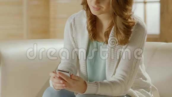 漂亮的女人坐在沙发上用手机给朋友发信息特写视频的预览图
