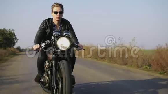 阳光明媚的一天一个穿着太阳镜和皮夹克骑摩托车的时尚酷青年的肖像视频的预览图