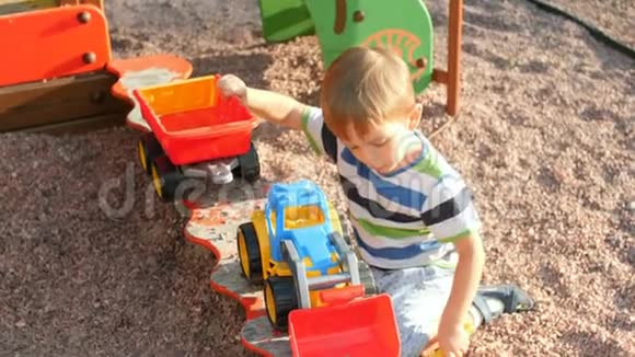 小男孩在沙箱里玩塑料玩具拖拉机和拖车的4k镜头视频的预览图