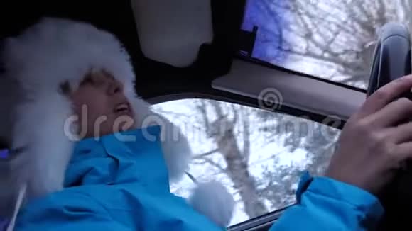 美丽而快乐的女孩在开车时跳舞和唱歌戴冬帽的女孩转动汽车方向盘视频的预览图