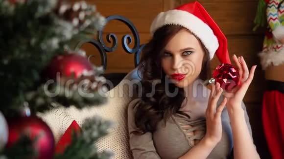 美丽的黑发圣诞老人戴着优雅的帽子和胸罩带圣诞树的室内模特儿时装画像视频的预览图