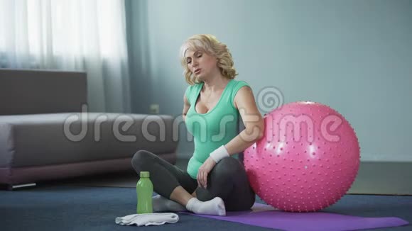 运动型高级女性坐在瑜伽垫上按摩背部腰痛视频的预览图