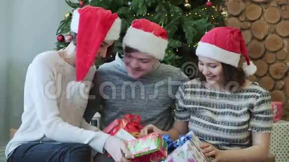 三个最好的朋友玩得开心拿着礼物坐在圣诞树附近特写镜头视频的预览图