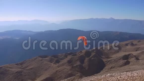 在阳光明媚的日子里滑翔伞在群山之间飞翔视频的预览图