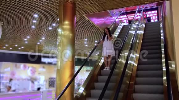 一个漂亮的女孩走下扶梯在商场里打电话视频的预览图