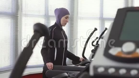 戴头巾的女孩在健身房的跑步模拟器上做热身运动健身训练视频的预览图