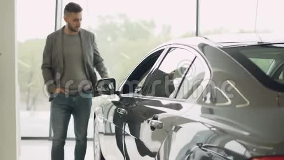 时尚的家伙正在选择新的汽车在豪华车周围走动并接触它在汽车经销商富人视频的预览图