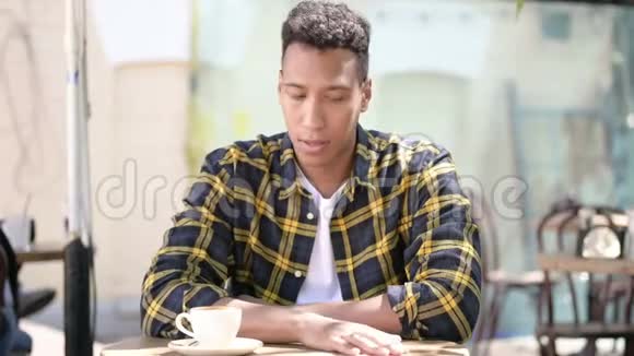 紧张的非洲年轻人头痛户外咖啡馆视频的预览图