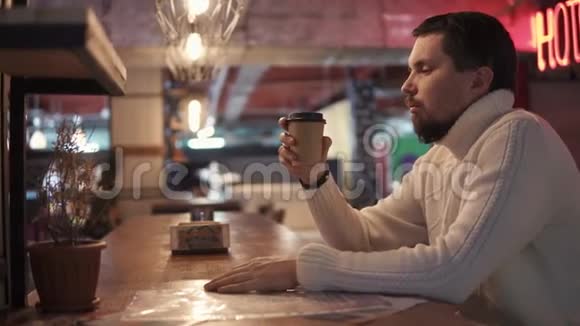 一个穿着暖和毛衣的年轻人从酒吧的纸杯里喝热咖啡视频的预览图