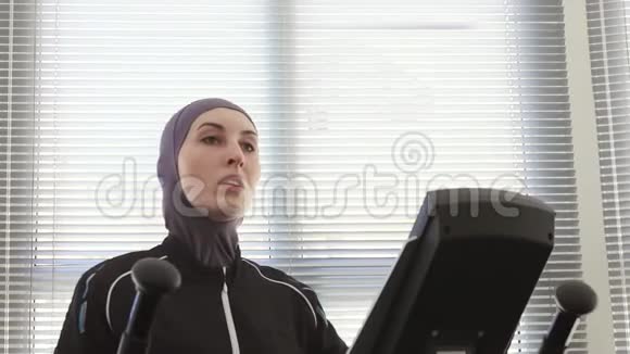 一名运动员女子在健身房的台阶模拟器上戴着头巾的肖像视频的预览图