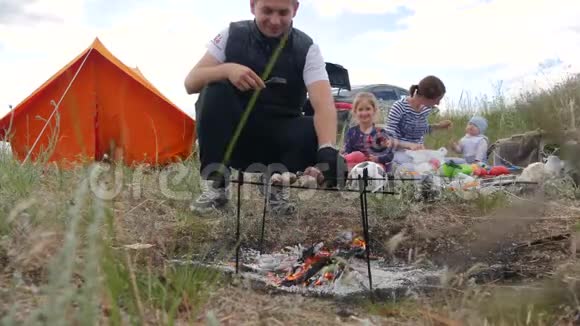 一个年轻而幸福的家庭她躺在草地上帐篷里烧着肉香肠妈妈抱着她视频的预览图