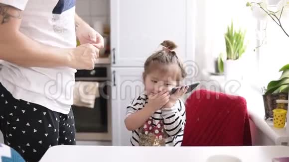 一个可爱的小女孩在打电话爸爸站在厨房附近视频的预览图
