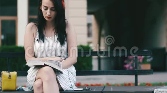 公园里可爱的女人头上戴红圈坐在长凳上读一本书视频的预览图