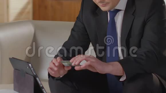 一个西装革履的男人在平板电脑上打信用卡号码付账单视频的预览图