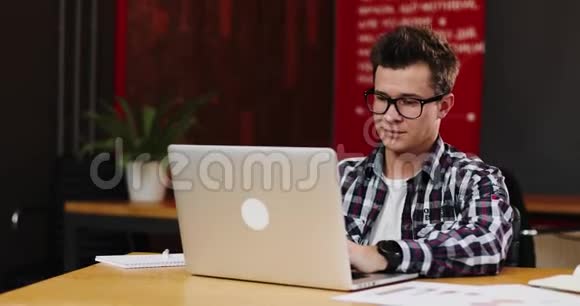 戴眼镜的严肃青年商人用笔记本电脑在现代办公室工作的画像视频的预览图