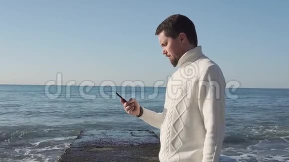 人手里拿着智能手机人站在海浪的背景上视频的预览图