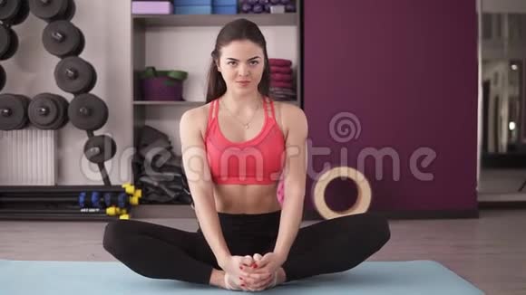 冷静的年轻女子在一个有哑铃的工作室里在瑜伽垫上展示伸展运动她在伸展身体视频的预览图