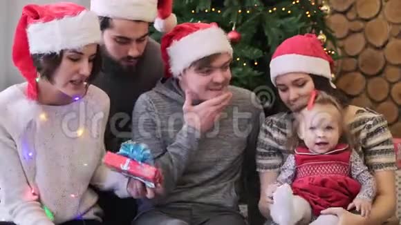 快乐美丽的家庭夫妇和他们的朋友一起坐在宝贝女儿身边在圣诞节前送给她不同的礼物视频的预览图