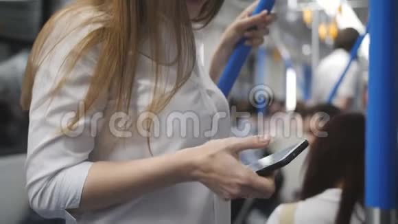 坐地铁的女人用智能手机一个女人坐在地铁车上紧紧抓住扶手一边走开视频的预览图