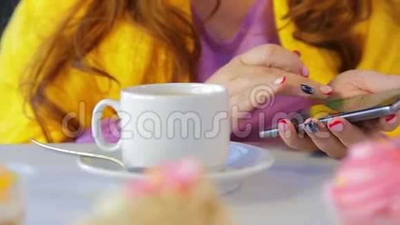 那个在桌旁的咖啡馆里吃蛋糕的女孩在智能手机里翻阅新闻视频的预览图