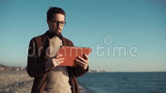 大胡子男子正在使用平板电脑坐在海滨城市全景视频的预览图