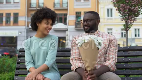 年轻男子把白色花束送给坐在长凳上的女人第一次尴尬的约会视频的预览图