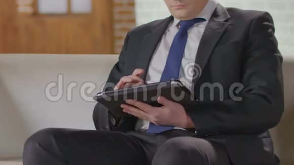 放松的商人坐在沙发上用平板电脑和打字午餐时间休息视频的预览图