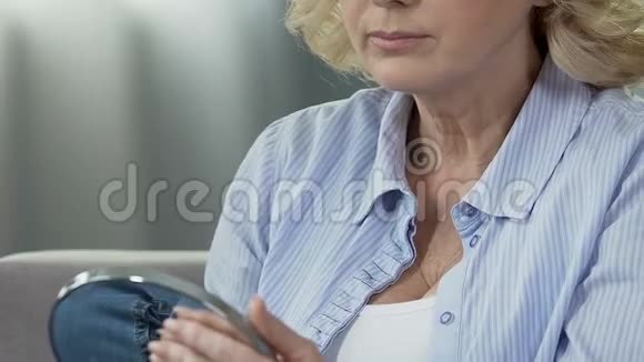 老妇人拿着镜子看着脖子摸着松弛的皮肤举起视频的预览图