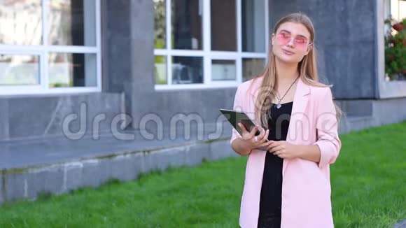 年轻的金发女郎在城里做平板电脑女性在街上使用无线互联网移动通信概念视频的预览图