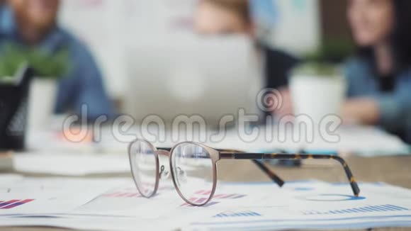 戴眼镜的财务图表和同事在后台开会视频的预览图