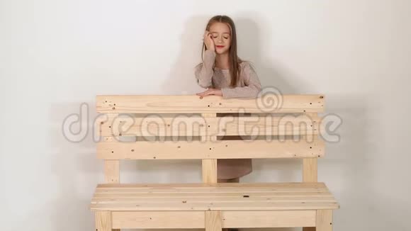 一个漂亮的小女孩穿着一件闪亮的米色连衣裙靠在一张木凳上视频的预览图