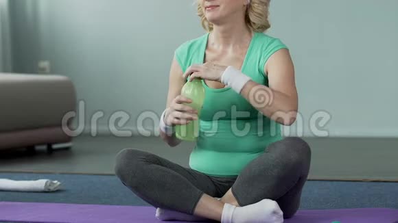 老年女性坐在健身垫饮用水体育活动上视频的预览图