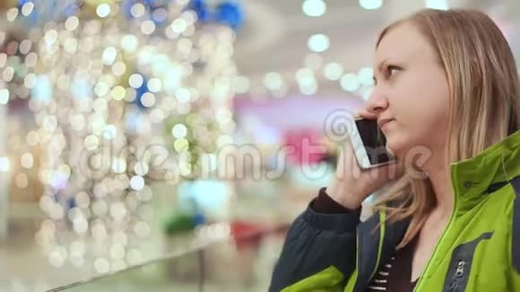 女人在智能手机上说话她正站在商场里一个灯泡不聚焦圣诞节的心情视频的预览图