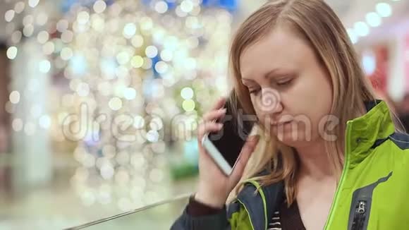 女人在智能手机上说话她正站在商场里一个灯泡不聚焦圣诞节的心情视频的预览图