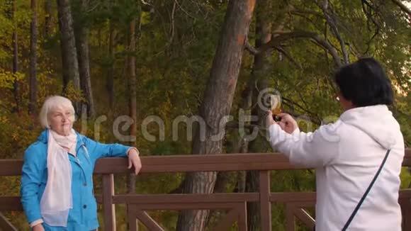 老年妇女拍摄朋友智能手机秋季景观视频的预览图